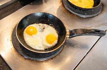 The cook is frying scrambled eggs in a frying pan in the kitchen.