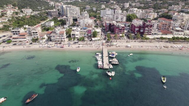 Spile Beach Coastline With Boat Pier In Himare Beside Turquoise Waters Of The Ionian Sea. Aerial Pan Left