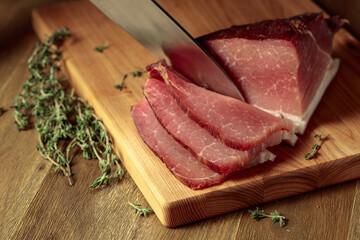 Dry-cured pork with thyme on a wooden cutting board.