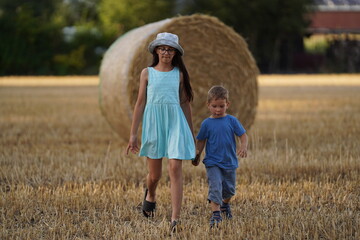 Two Children brother and sister on a hay field at the sunset