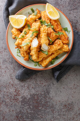 Battered and fried golden squid strips with lemon closeup on the plate on the table. Vertical top view from above