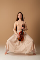 Portrait of a girl with a violin and a bow in her hands on a plain beige background. Music concept