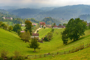 Rural idyllic landscape of the small villages in the Rucar-Bran mountain area, Brasov, Romania, scattered on the wooded hills, with the Bucegi mountains in the background, in wonderful springtime day