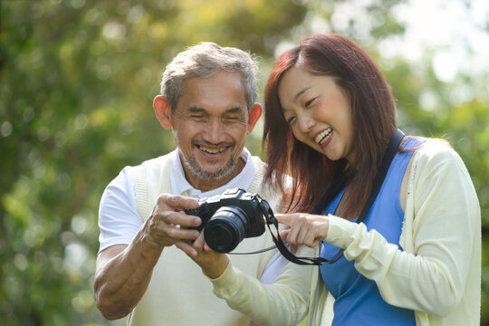 young asian daughter enjoy outdoor activity together with retired senior father, they are looking at pictures on a  camera,concept family relationship, lifestyle, relaxing, travel
