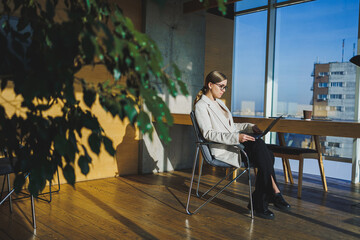 Successful young business woman in glasses with laptop in office. Business woman sending email message and working on laptop. Young business woman sitting at workplace