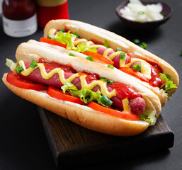 Hot dog with grilled sausage, tomato and lettuce on dark background. American hotdog