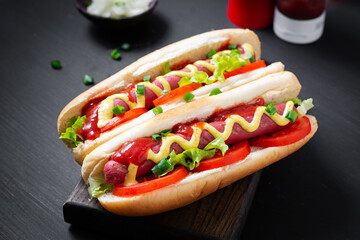 Hot dog with grilled sausage, tomato and lettuce on dark background. American hotdog