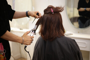 女性の髪にヘアアイロンをかける男性美容師