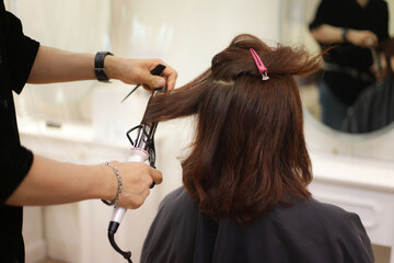 Obraz na płótnie Canvas 女性の髪にヘアアイロンをかける男性美容師