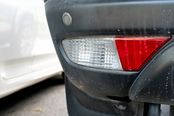 Back of a car that is soiled with dust. On back of car with white and red rear lights for reversing...