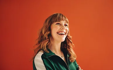 Fotobehang Happy young woman looking away with a smile while standing in a studio © Jacob Lund