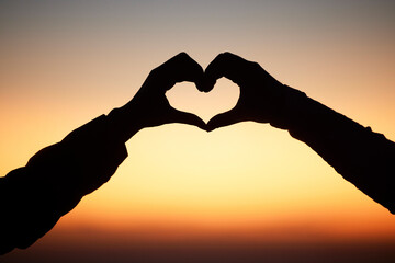 Sunset, hands in heart and silhouette of couple at beach for romantic vacation, holiday and adventure. Emoji, travel and sky shadow of people relax, calm and together for trust, commitment and love