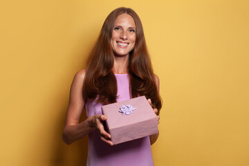 Happy joyful woman holding pink gift present box on bright yellow background