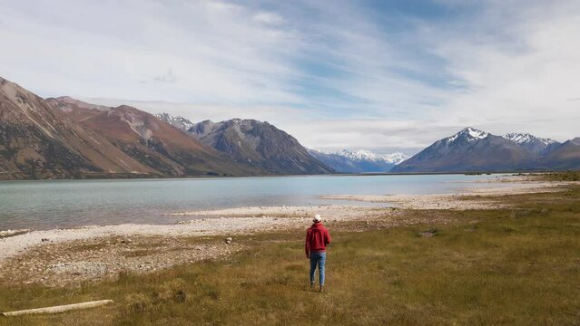 Person from behind walking towards beautiful glacier lake in front of picturesque, alpine scenery