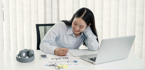 Asian woman working laptop. Successful smiling businesswoman sitting working and taking notes at the office