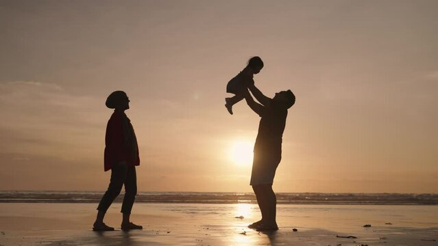Silhouette of Father Mother and Child in Slow Motion. Happy Modern Muslim Indonesian Family Enjoying Sunset Together on The Beach.