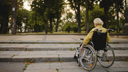 Senior woman in wheelchair near the curb in the street, accessibility of city
