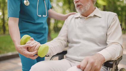 Traumatologist assisting aged man with rehabilitation therapy, exercising with dumbbells