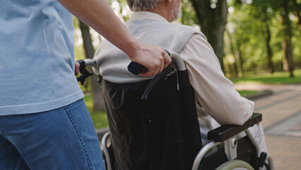 Fototapeta na wymiar Caretaker pushing senior man's wheelchair, life with disability, retirement