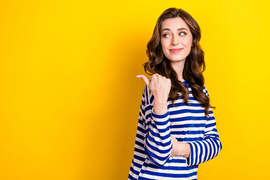 Photo of young pretty lovely brown wavy hair lady wear striped pullover directing finger empty space new brand isolated on yellow color background