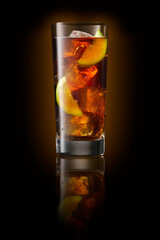 cola cocktail in tall glass with ice cubes and lemon