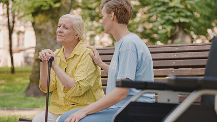 Helpful volunteer supporting sad old woman sitting on bench with a walking stick