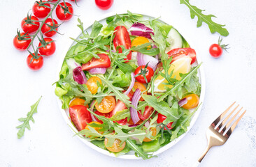 Fresh spring vegan vegetables salad with colorful cherry tomatoes, cucumber, red onion, lettuce, radicchio and arugula. White table background, top view
