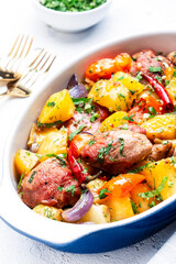 Baked turkey drumsticks ragout with potatoes, paprika, onions, herbs and spices in baking dish, white table background, top view