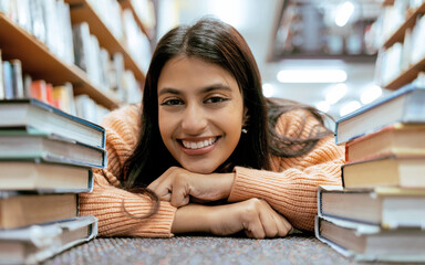 Portrait, Indian woman on floor and books to relax, smile and hobby for learning, growth and...