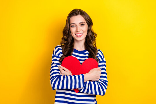 Photo of optimistic woman wear striped blue jumper embrace her red paper love symbol valentine day february gift isolated on yellow color background
