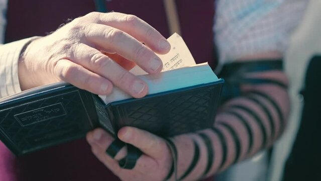 An elderly man with tefillin on his hand prays with a Torah scroll in his hands