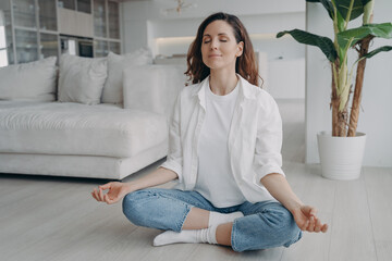 Caucasian woman is sitting in lotus asana at home in morning. Scandinavian interior of living room.