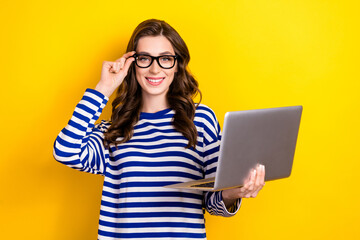 Photo of cheerful smiling woman wear striped pullover use computer glasses hold laptop enjoy remote education isolated on yellow color background