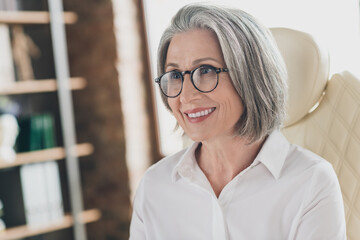 Photo of positive cheerful aged lady company founder sit leather chair toothy smile spacious bright office indoors