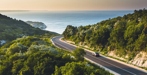 Driving on a coast road. Aerial view of a car driven on an amazing curved waving road at the Sea...