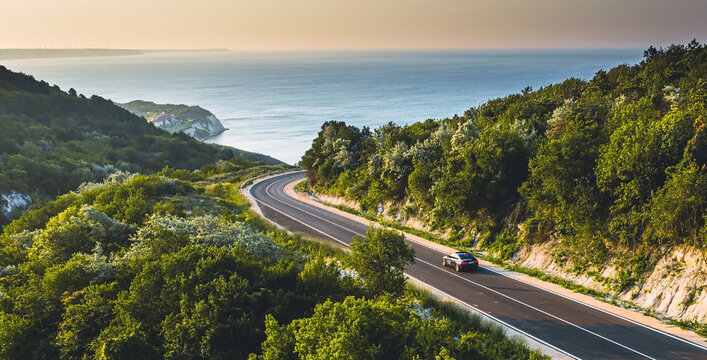 Driving on a coast road. Aerial view of a car driven on an amazing curved waving road at the Sea shore in Balchik sea resort in Bulgaria.