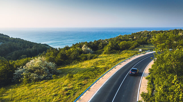 Driving on a coast road. Aerial view of a car driven on an amazing curved waving road at the Sea shore in Balchik sea resort in Bulgaria.