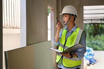 Asian male civil engineer manager standing at construction site and communicating with walkie talkie 