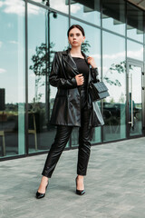 Naklejka premium Pretty brunette caucasian woman dressed leather suit with shoulder bag walking outside street. Businesswoman hurry to work. Office CEO clerk. Confident serious lady. Professional business owner 