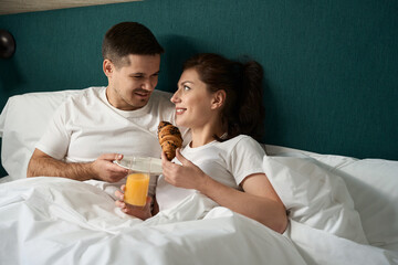 Young spouses have breakfast in bed in a hotel room