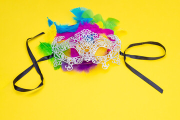 Venetian carnival lace white mask with ribbons and colorful feathers on a yellow background.