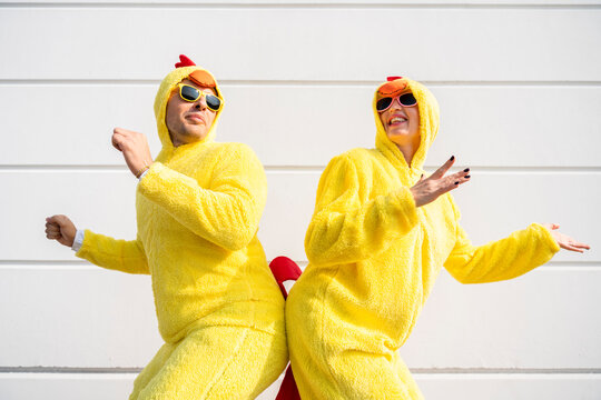 Happy woman and man wearing yellow chicken costumes having fun in front of wall