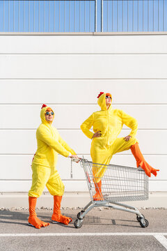 Friends wearing chicken costumes standing with shopping cart in front of wall