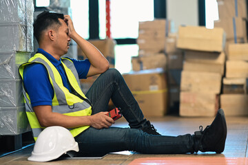 Tired man warehouse worker in jacket leaning against metallic rack while having short break