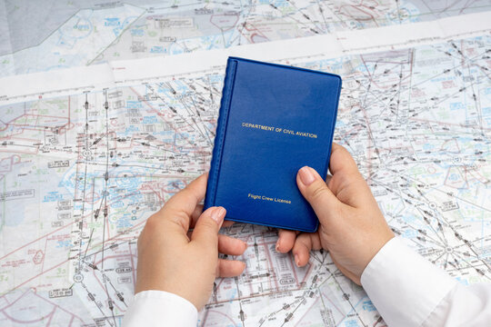 A woman holds a pilot's license in her hands against the background of navigation charts. The concept of a female pilot