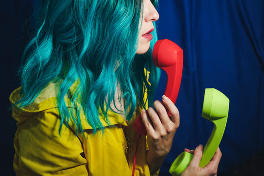 Woman with dyed hair holding red and green telephone receivers in front of blue backdrop