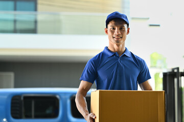 Portrait of delivery man carrying cardboard parcel and smiling at camera. Delivery service, post and shipping concept