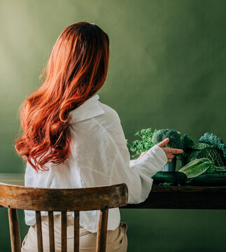 Redhead woman sitting with fresh vegetable in front of wall