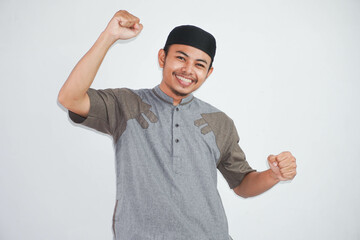 Confident cheerful handsome asian muslim man lifting hands up wearing koko clothes feels happiness...