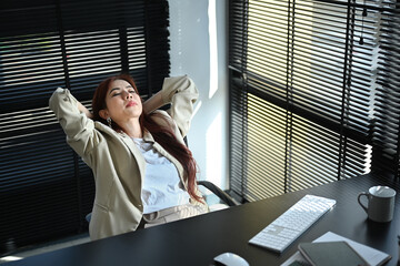 Millennial businesswoman relaxing on office chair with her eyes closed and her hands behind her head